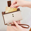 A hand is inserting a card into a brown leather multi-slot wallet with a gold zipper and a leather strap.