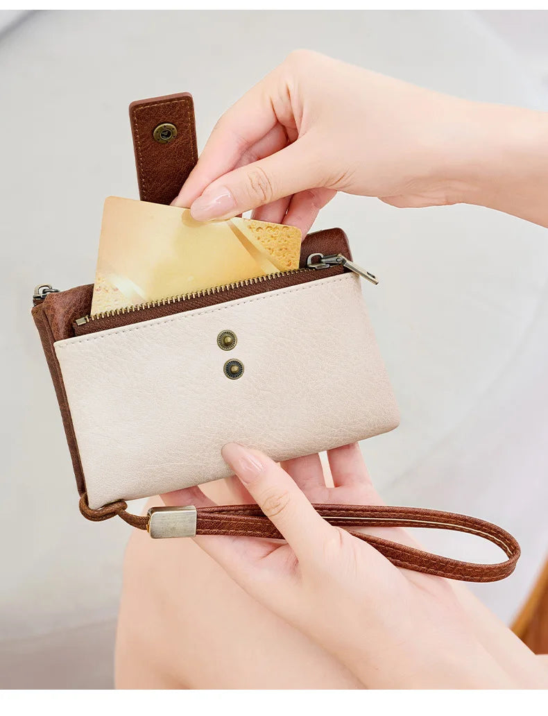 A hand is inserting a card into a brown leather multi-slot wallet with a gold zipper and a leather strap.