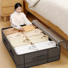 A woman is placing a folded yellow item into a black under-bed storage box with a window next to a wooden bed frame.