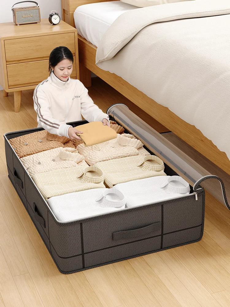 A woman is placing a folded yellow item into a black under-bed storage box with a window next to a wooden bed frame.