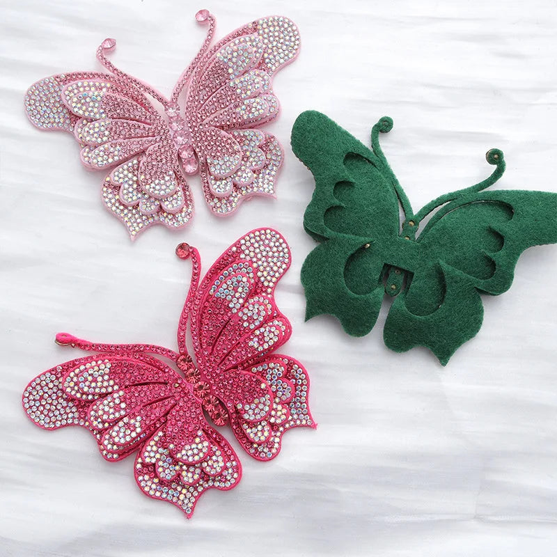 Two decorative rhinestone butterfly appliqués in pink and green on white fabric.