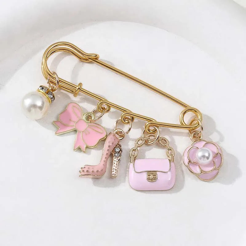 A gold-toned chain accessory featuring a pearl, a pink bow, a silver stiletto, and a light pink purse charm.