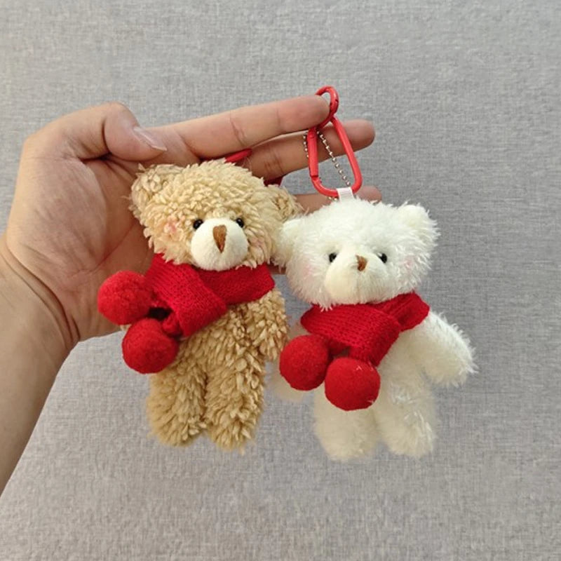 A hand holds a fluffy brown teddy bear and a white teddy bear, both with red scarves, as a keychain.