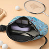 A blue and white doodle print crossbody waist bag with a zippered compartment and a silver-framed mirror, resting on a light 