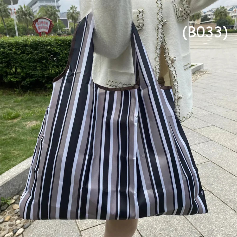A black and white striped foldable oxford grocery tote bag carried by a person.