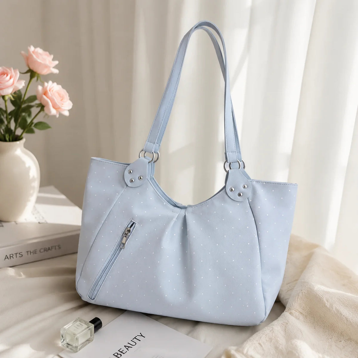 Light blue retro polka dot shoulder tote bag resting on a white surface next to a pink flower and skincare product.