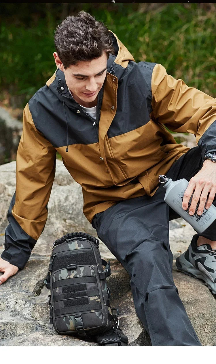 A male model wearing a tan and black tactical jacket and dark pants, holding a gray water bottle outdoors.