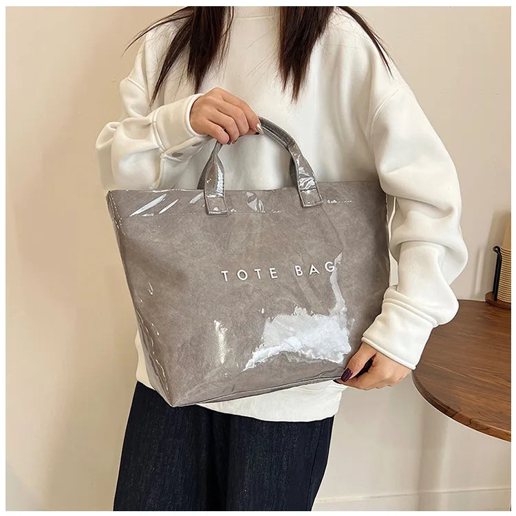 A person holds a gray transparent waterproof PVC tote bag against a light background.