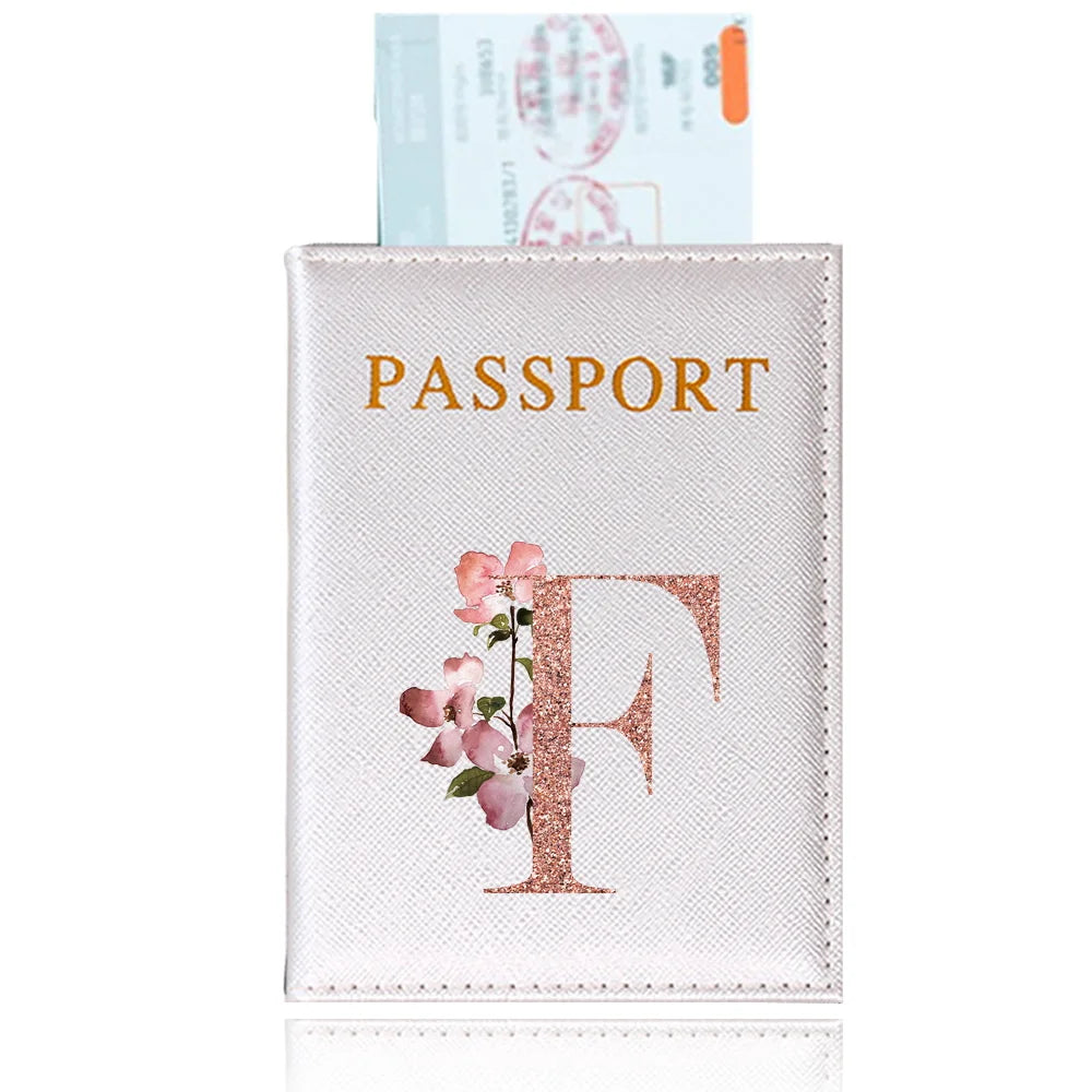 A pink leather passport holder featuring a gold foil initial F and floral accents.