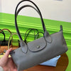 A hand holds a gray leather shoulder bag with black handles against a bright green background.