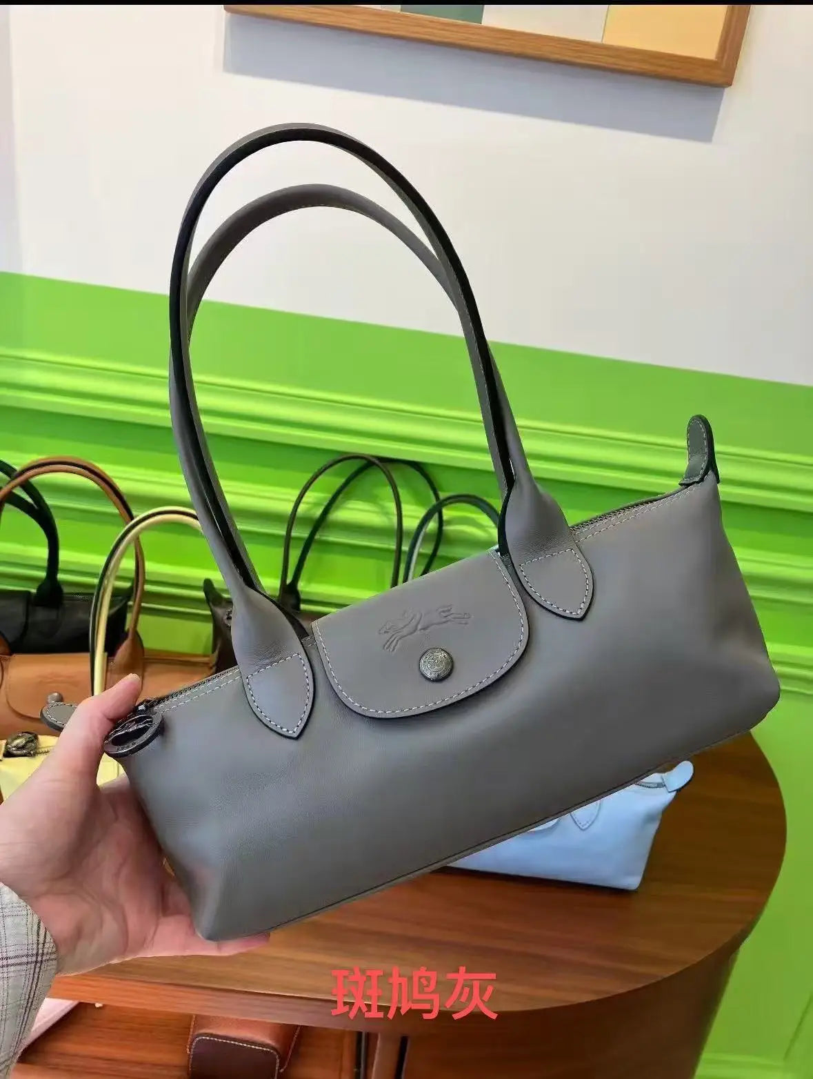 A hand holds a gray leather shoulder bag with black handles against a bright green background.