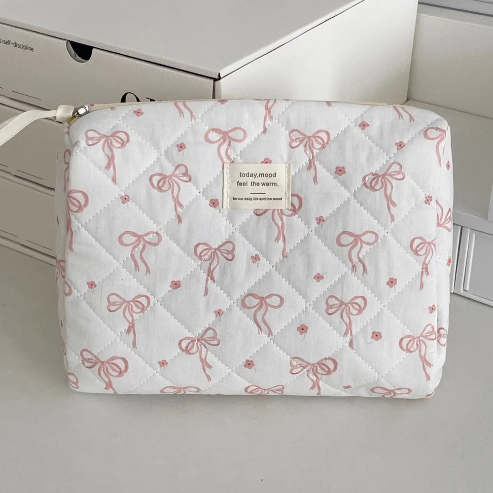 A white quilted cosmetic bag with pink ribbon embroidery resting on a light surface.
