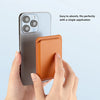 A hand holds a brown leather MagSafe magnetic card holder wallet against a silver iPhone.