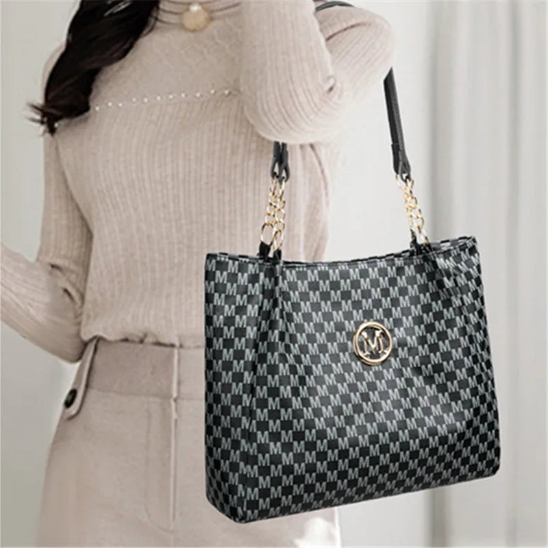 A woman holds a black and white geometric letter M tote bag with gold hardware against a light background.