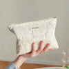 A hand holds a cream-colored floral canvas makeup bag with a small tag against a light background.
