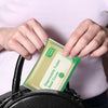 Hands are placing a green disposable toilet seat cover onto a black bag.