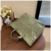 A green transparent waterproof PVC tote bag resting on a wooden table next to a vase of yellow flowers.