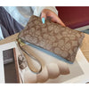 A brown crocodile print zipper long multi-card wallet is shown lying on a white tray with some beige cosmetic products.