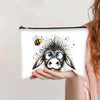 Una mano sostiene una bolsa de cosméticos con cremallera que presenta un dibujo detallado en blanco y negro de la cara de una