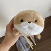 A light brown otter plush toy with a white mustache is being held by a hand.
