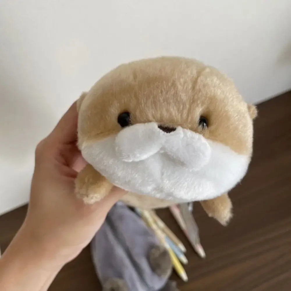 A light brown otter plush toy with a white mustache is being held by a hand.