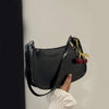 A black PU leather shoulder bag with a gold chain and cherry pendant is held by a hand against a white background.