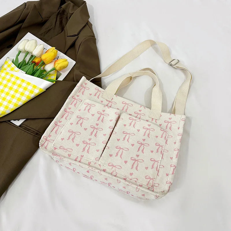 A light pink canvas tote bag with a repeating strawberry ribbon pattern is shown next to a green and yellow checkered paper, 
