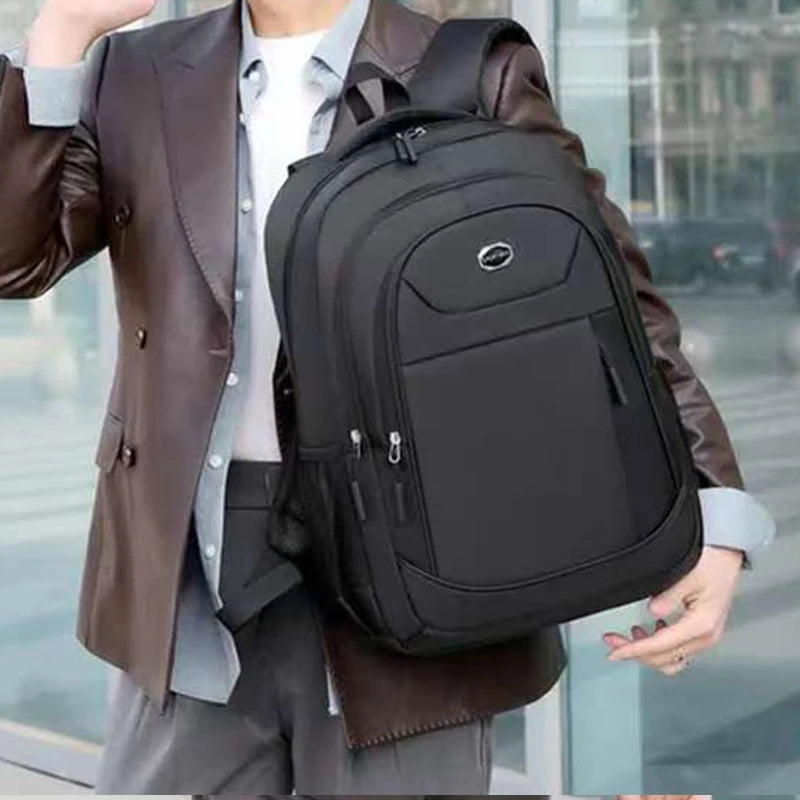 A person is holding a black unisex double-shoulder travel backpack while wearing a brown leather jacket and light shirt.