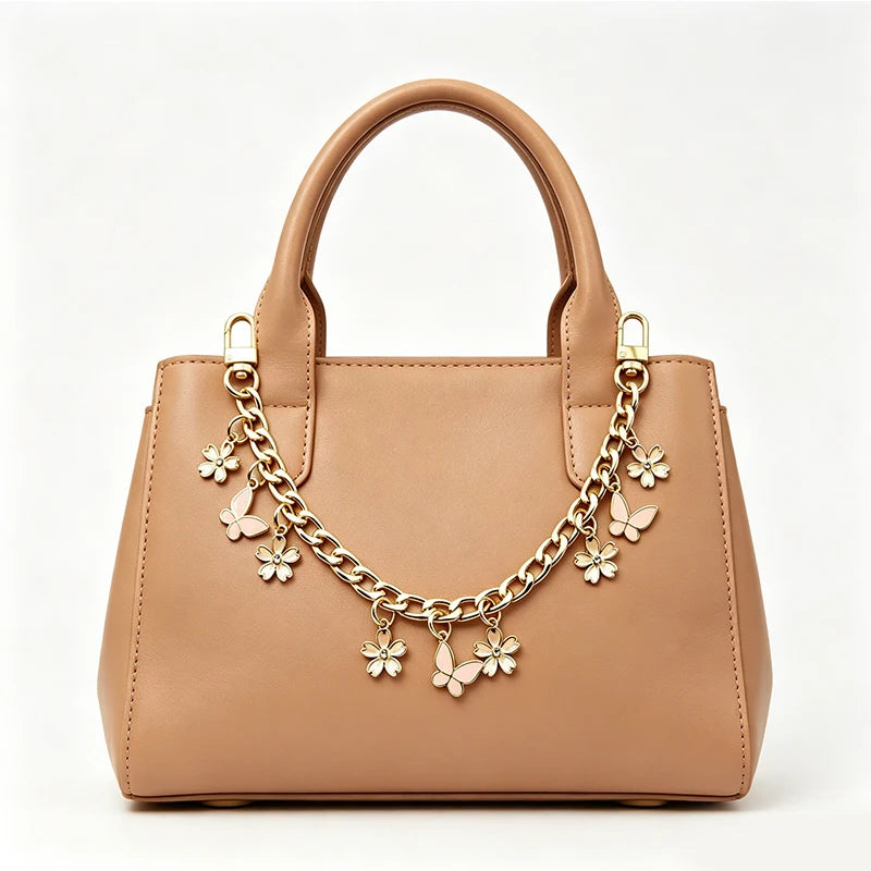 A tan leather handbag with a gold chain and flower pearl charm extension necklace.