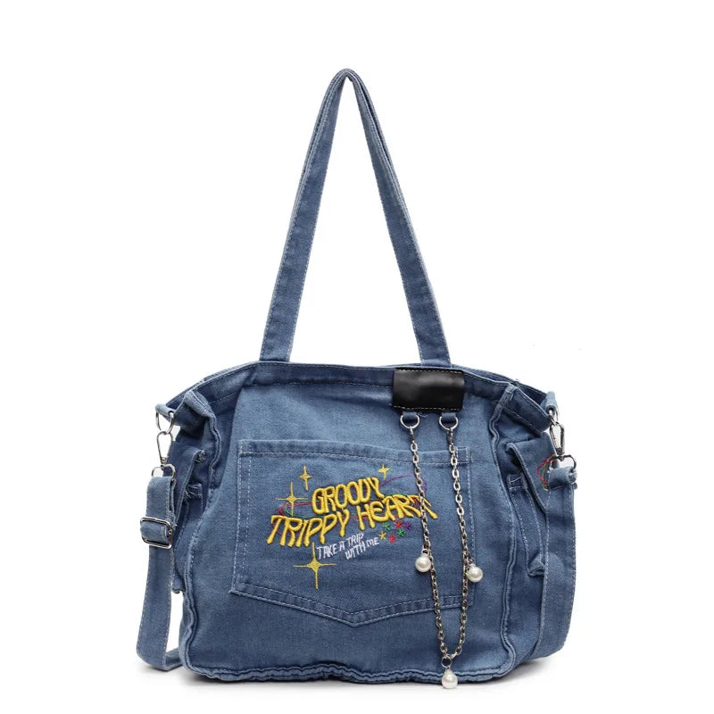 A denim crossbody bag featuring embroidered text and a black leather accent.