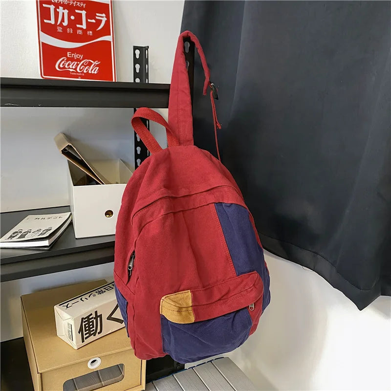 A red and blue canvas fashion backpack hanging on a shelf next to a Coca-Cola sign.