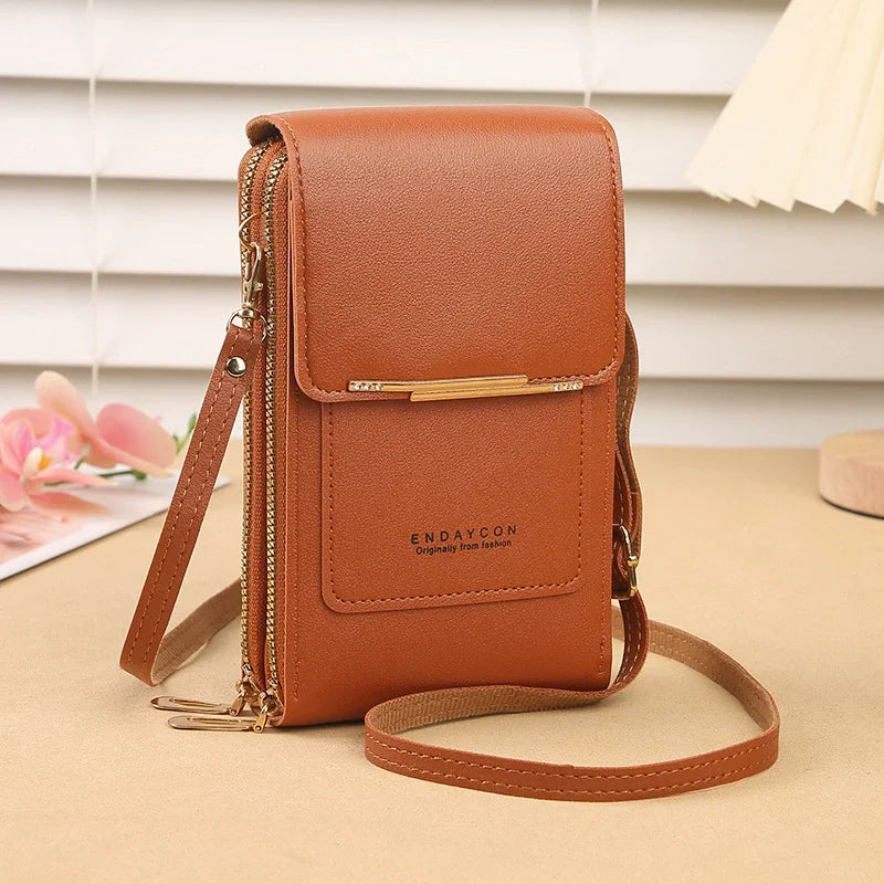 A tan leather crossbody shoulder bag with gold hardware and a flap closure resting on a beige surface.