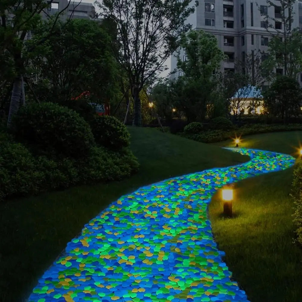 A winding pathway decorated with glow-in-the-dark solar pebbles in shades of blue, green, and yellow through a lush garden.