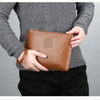 A person holds a brown PU leather men's clutch wallet against a gray sweater and black pants.
