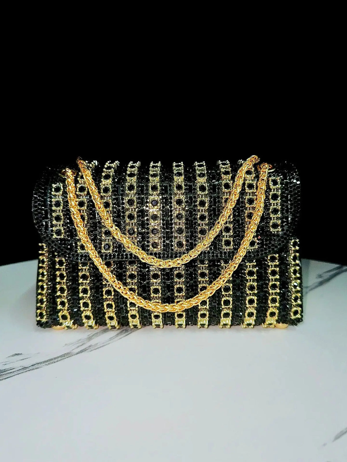 A black clutch bag adorned with gold-toned rhinestone detailing and a gold chain strap.