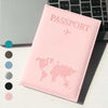 A pink slim PU passport holder with a embossed world map design is shown next to a laptop keyboard.