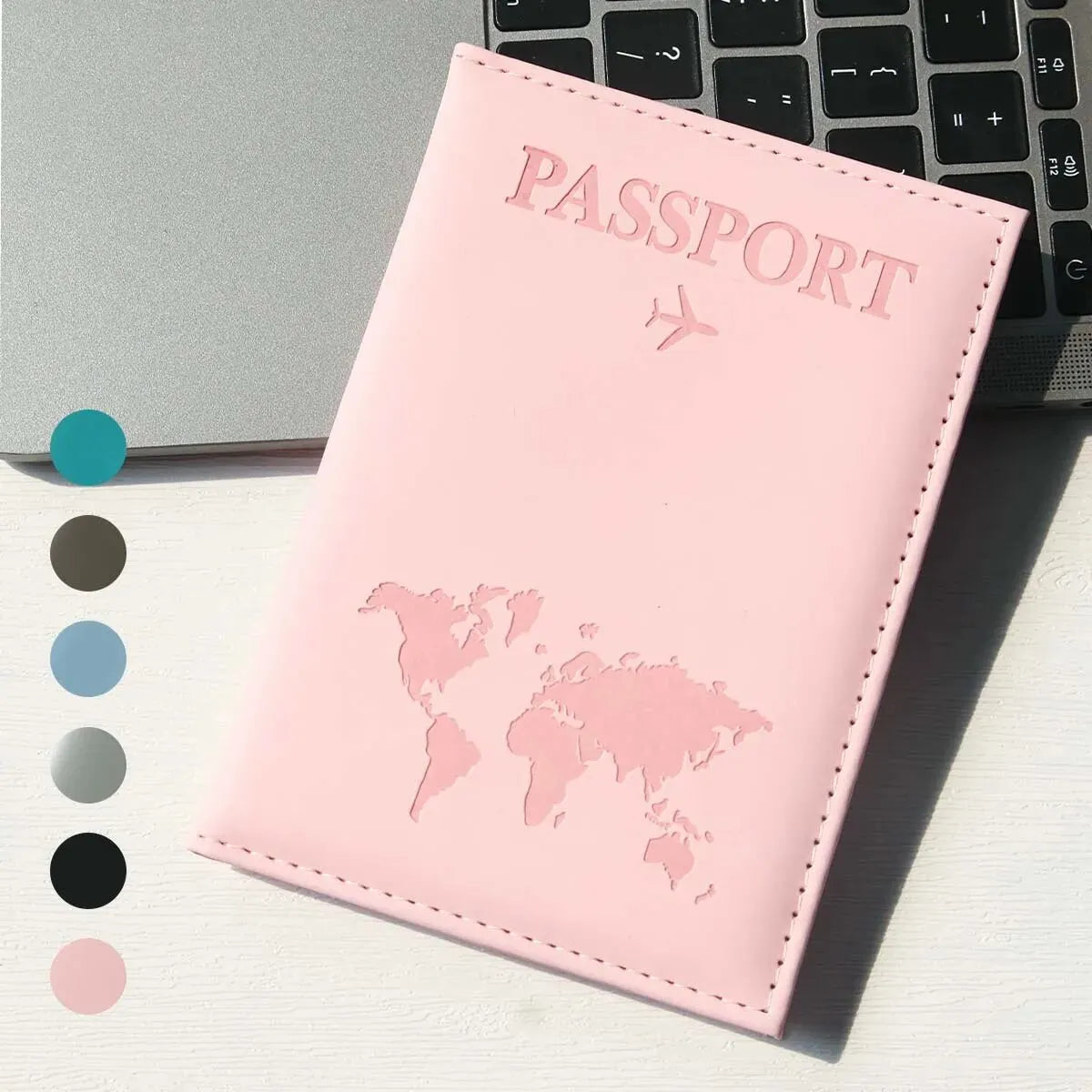 A pink slim PU passport holder with a embossed world map design is shown next to a laptop keyboard.