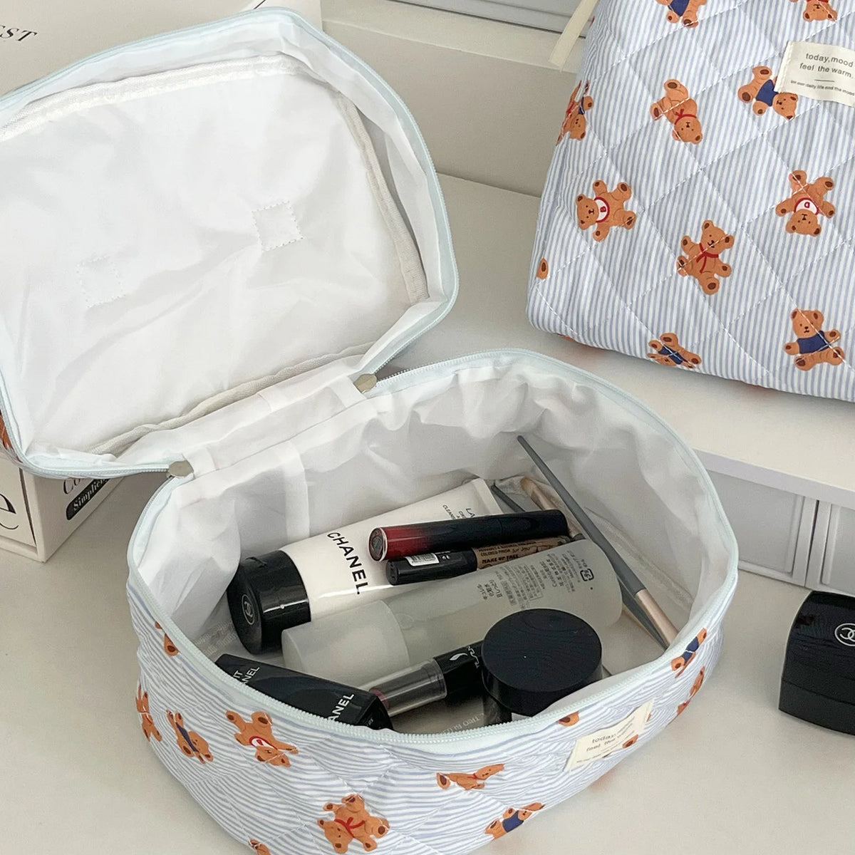 A white cosmetic makeup bag with a striped pattern is open, revealing various makeup and grooming tools inside.