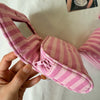 A hand holds a pink striped makeup bag with a flip-top mirror.