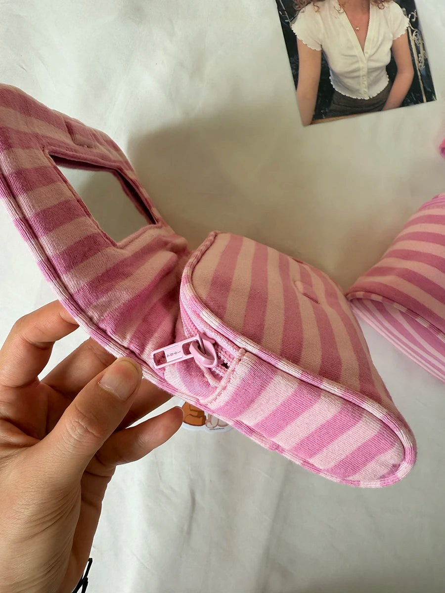A hand holds a pink striped makeup bag with a flip-top mirror.
