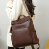 A woman is wearing a brown vintage tassel backpack over a cream blazer and black pants.