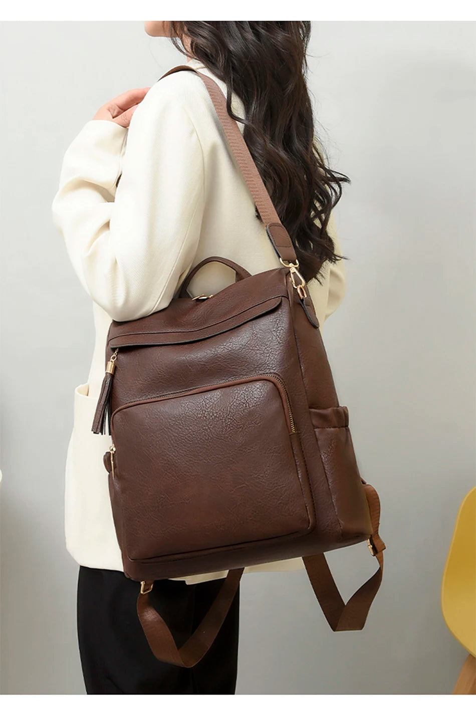 A woman is wearing a brown vintage tassel backpack over a cream blazer and black pants.
