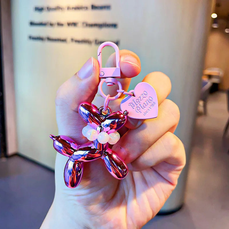 A hand holds a purple glitter balloon dog keychain charm with a pink padlock and a heart tag.