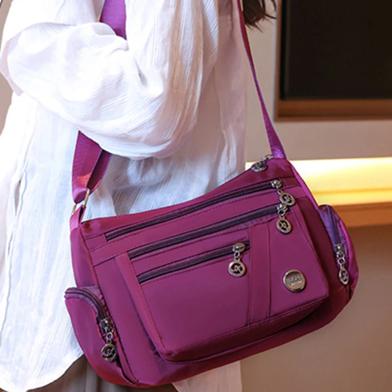 A magenta waterproof nylon crossbody tote bag being held by a person, shown from the side.