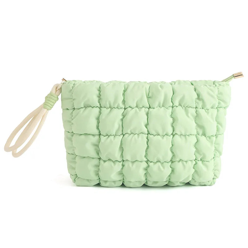 A light green quilted puffer makeup bag with a fabric strap is shown.