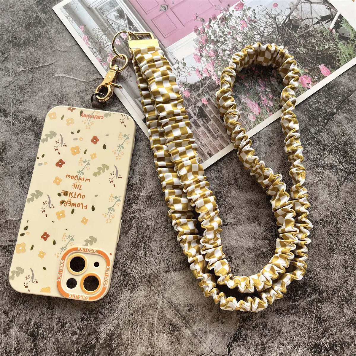 Elegante goldene Schlüsselkette mit geflochtenem Gold- und Cremkord neben einem Telefon.