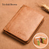 A tri-fold brown leather wallet resting on a brown surface with a feather in the background.