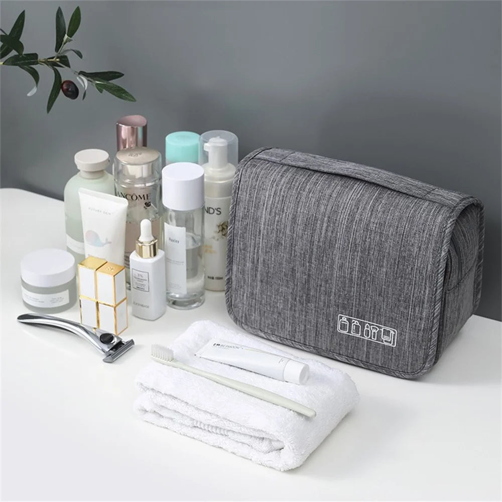 A gray portable waterproof toiletry washbag is shown with various skincare and grooming products arranged around it.