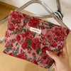 A red floral patterned cosmetic pouch is held in a hand, resting on a glass or metal frame.