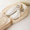 A pair of white canvas shoes is placed inside a beige portable luggage shoe organizer bag.